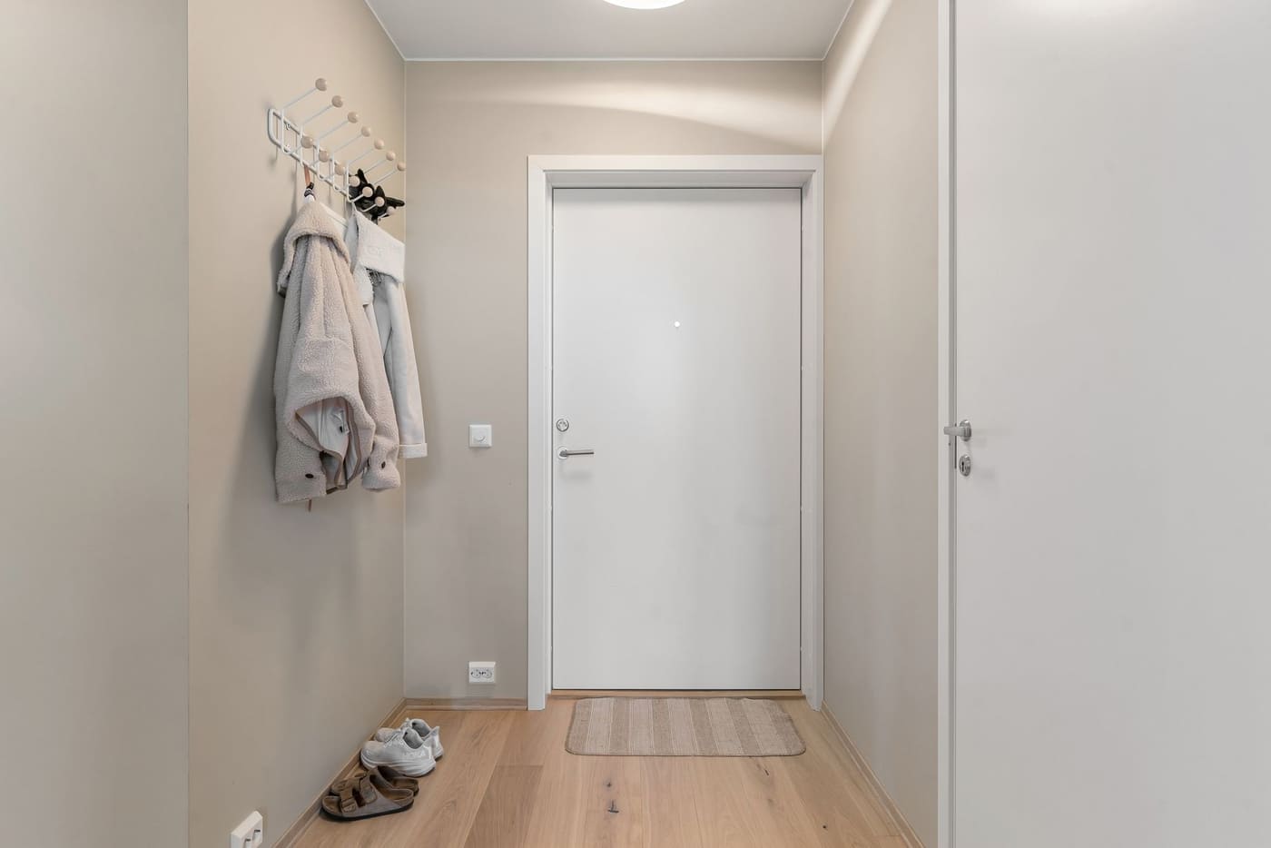 A bright apartment entrance with a few jackets on a wall hook rack beside the door