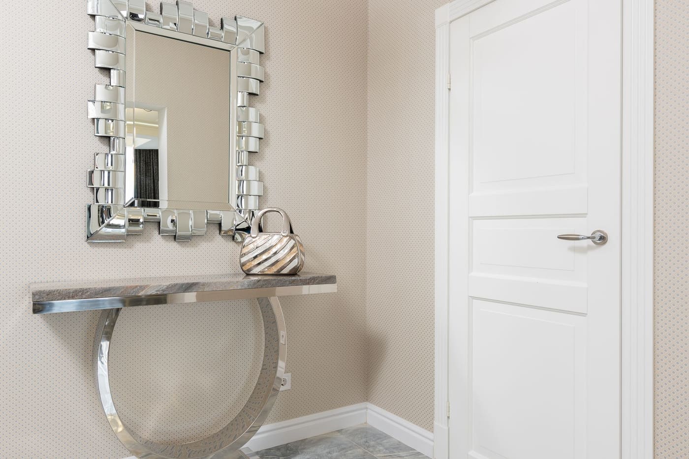 A narrow wall-mounted console with a patterned mirror above it and a handbag resting on top