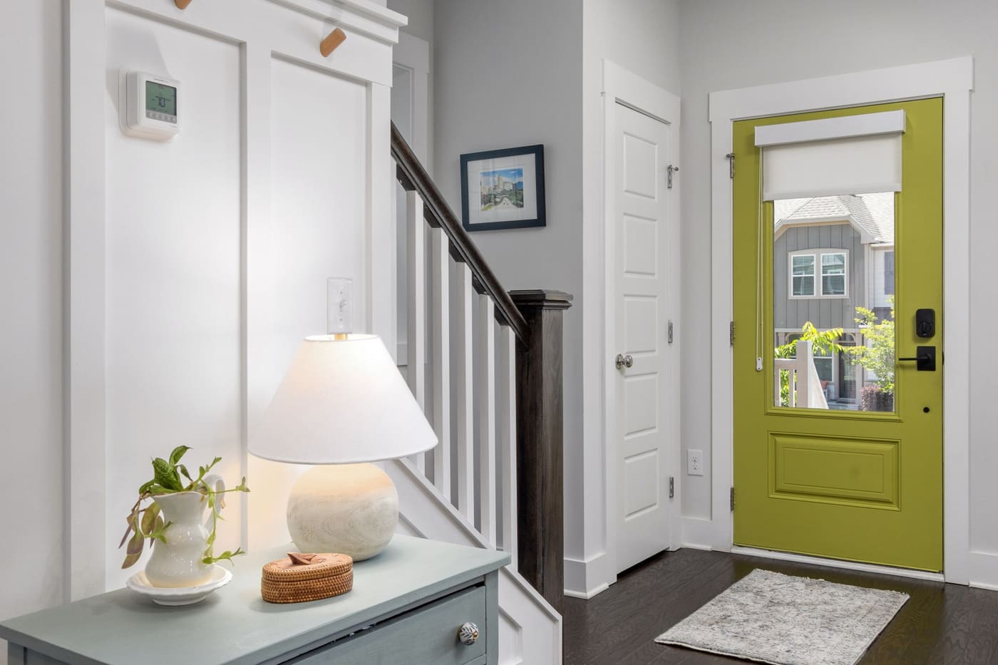 A small entry with a green door, a console with a lamp and a plant, and a patterned mat