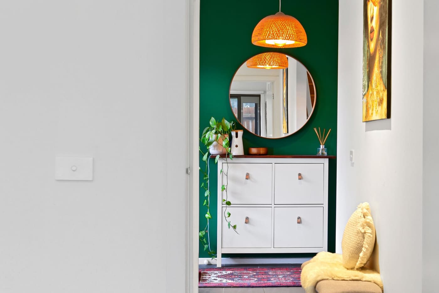 A small entry with a green accent wall, a round mirror and a white tilting shoe cabinet with drawers