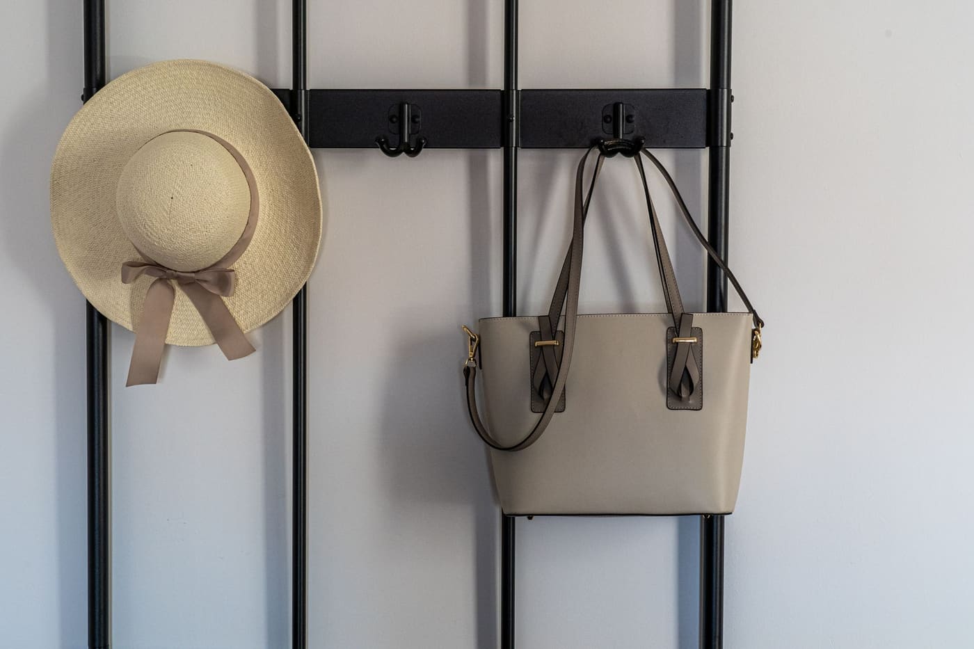 A straw hat and a leather handbag hanging from a black wall hook