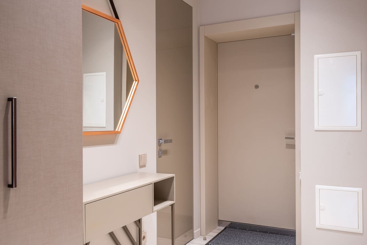 A hexagonal mirror above a small console in a corridor with beige doors