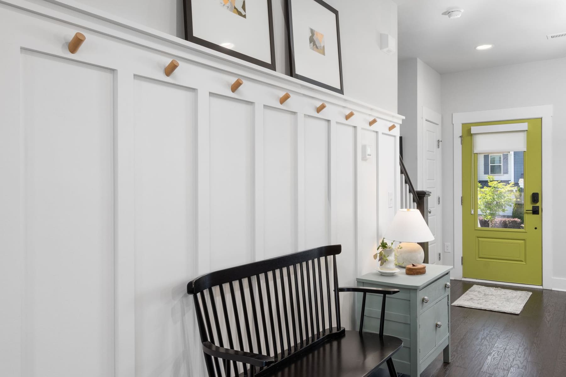 A bright entryway with a wall of hooks, a wooden bench and a green front door