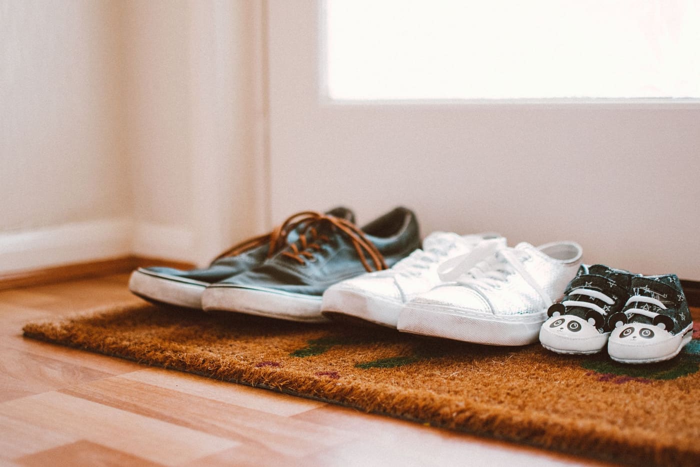 Three pairs of shoes lined up on a coir doormat just inside a doorway