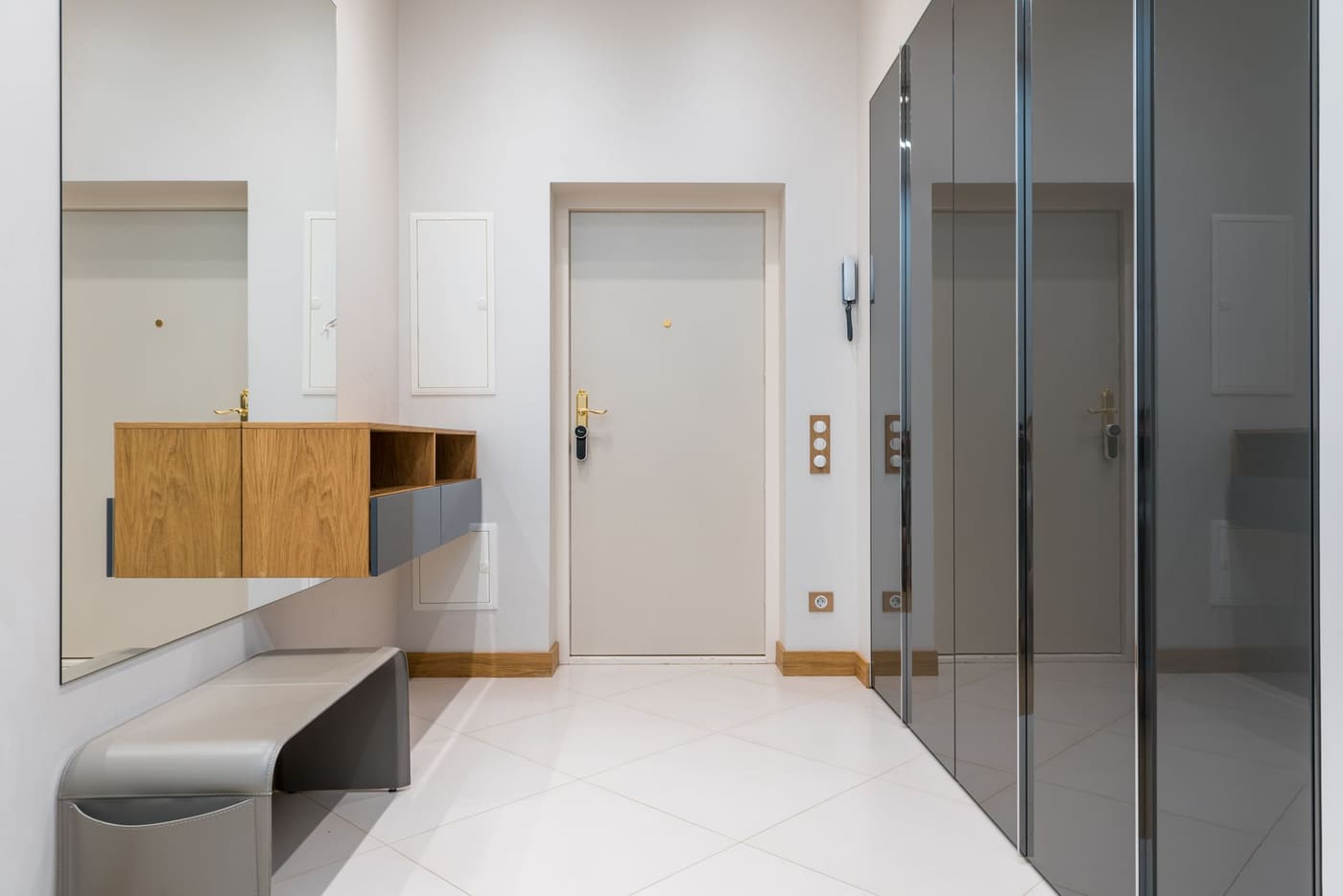 A compact entry with a wall-mounted wooden shelf above a low grey bench beside mirrored wardrobe doors