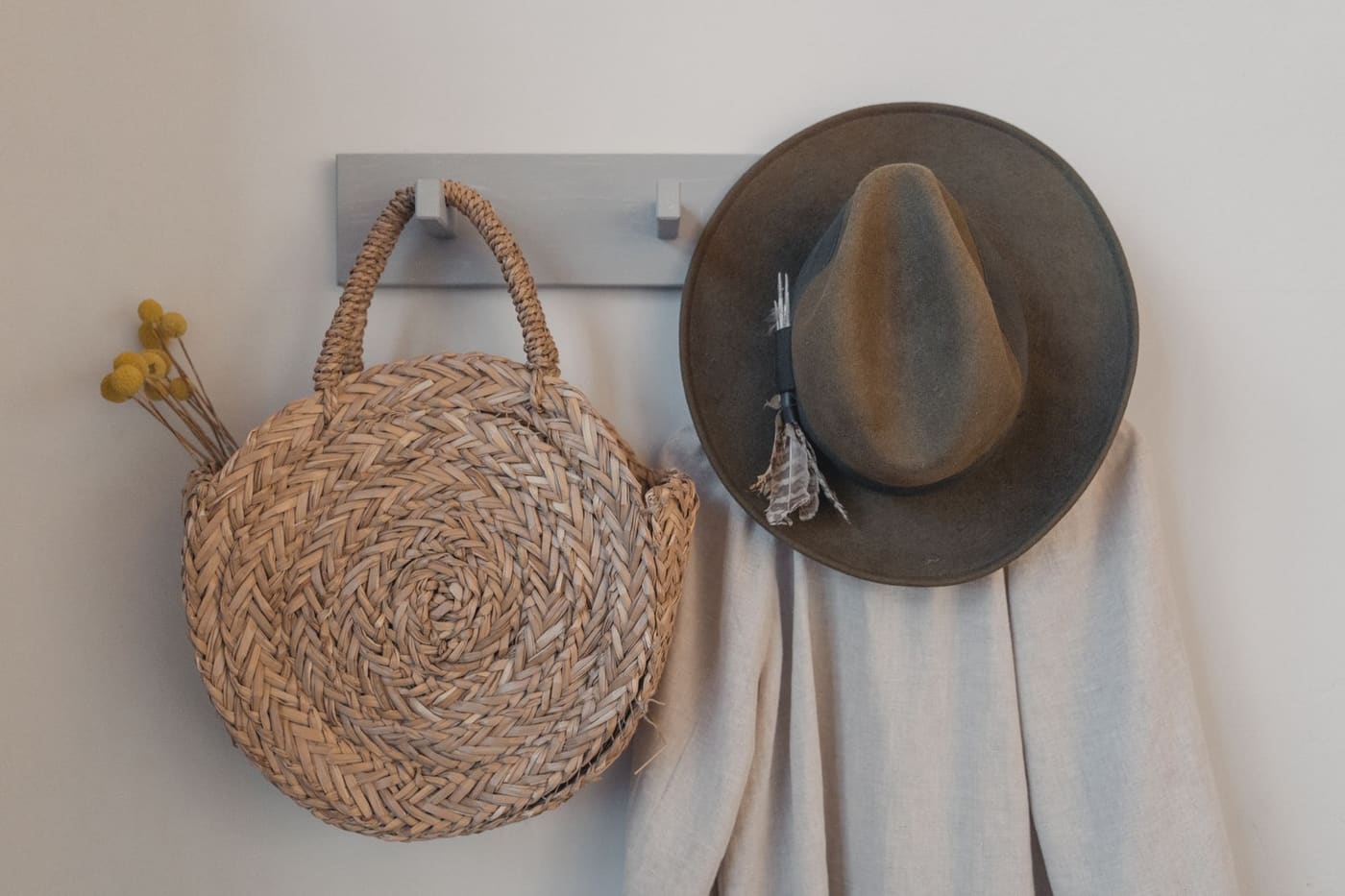 A woven round bag and a felt hat hanging from a simple wall hook rail